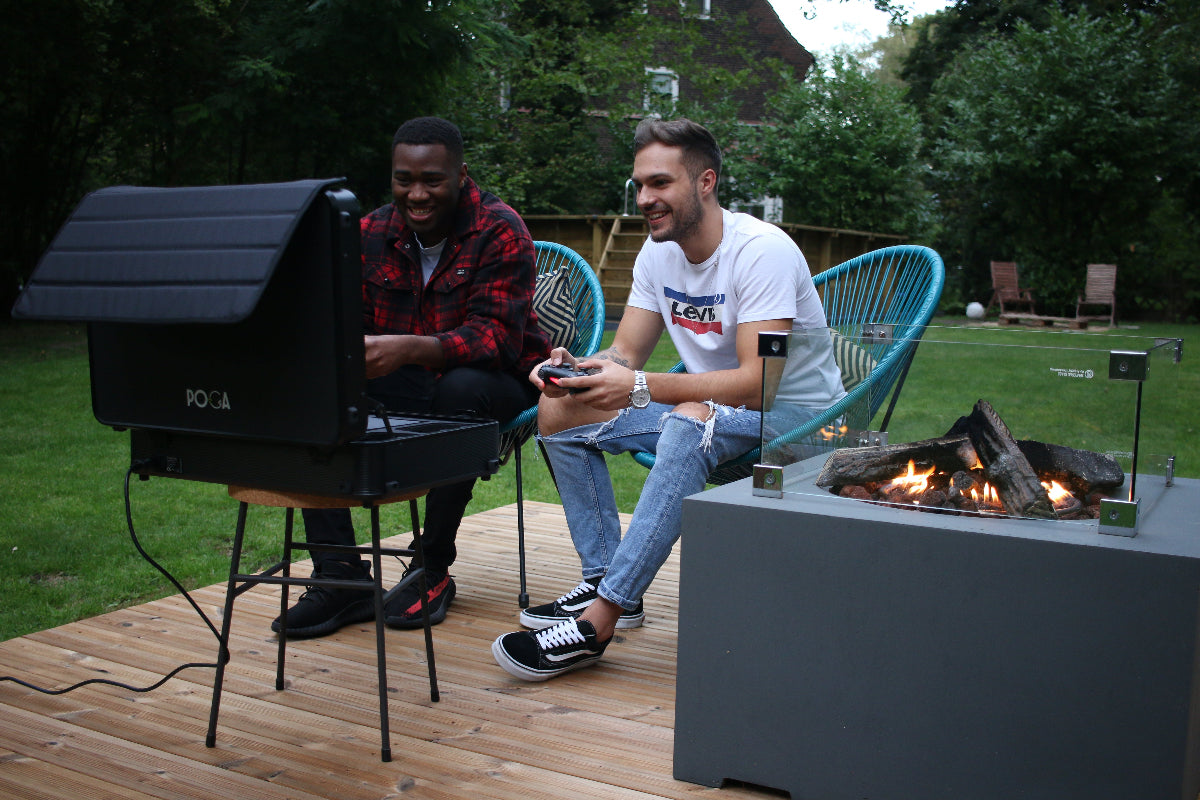 Two men sitting by a fire pit on a wooden deck with a television set.