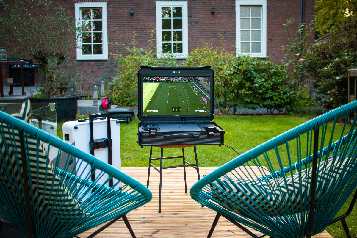 Portable outdoor TV on a stand with a sports game displayed, surrounded by green chairs and a house in the background.