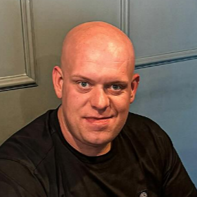 Man with a bald head wearing a black shirt against a plain background