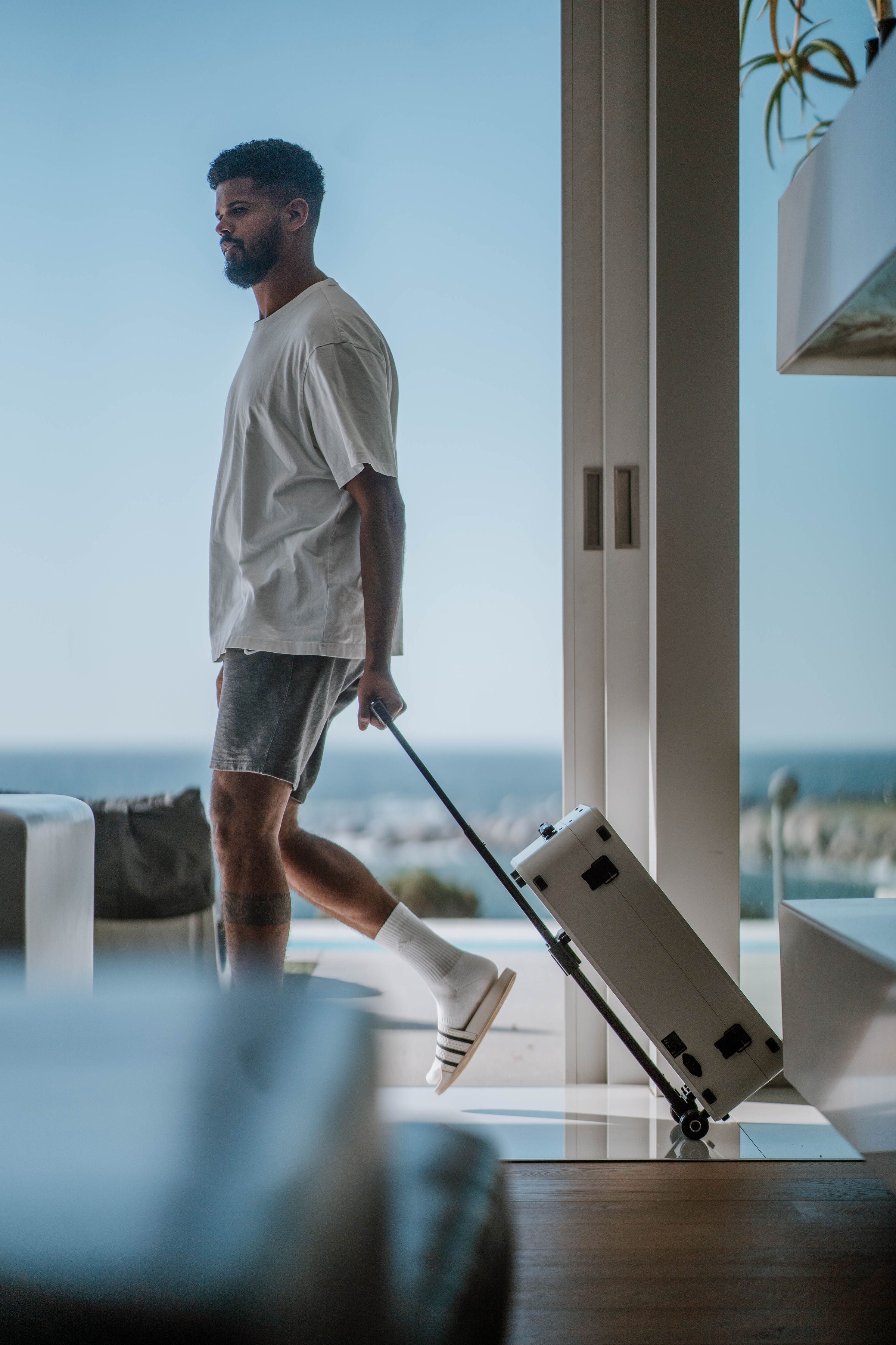 Man with a poga gaming suitcase standing by a large window with a view of the ocean.
